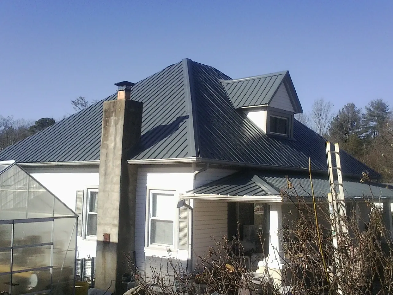 Dark blue standing seam metal roof on a white farmhouse with dormer — Slate & Tile Roof Repair by Roofing Brothers in Asheboro