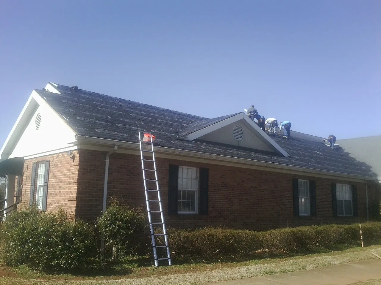 Crew tearing shingles off a brick ranch roof with a ladder set — Emergency Roof Repair work by our crew in Asheboro