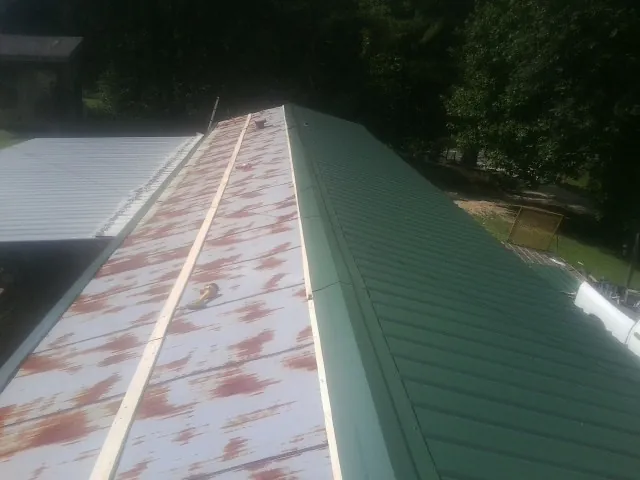 Old rusted panels beside newly installed green metal roofing — Wind Damage Roof Repair by Roofing Brothers in Asheboro