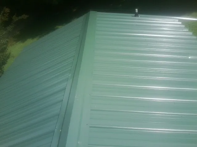 New green metal panels meeting at the ridge of a roof — Flat Roof Repair work by our crew in Asheboro