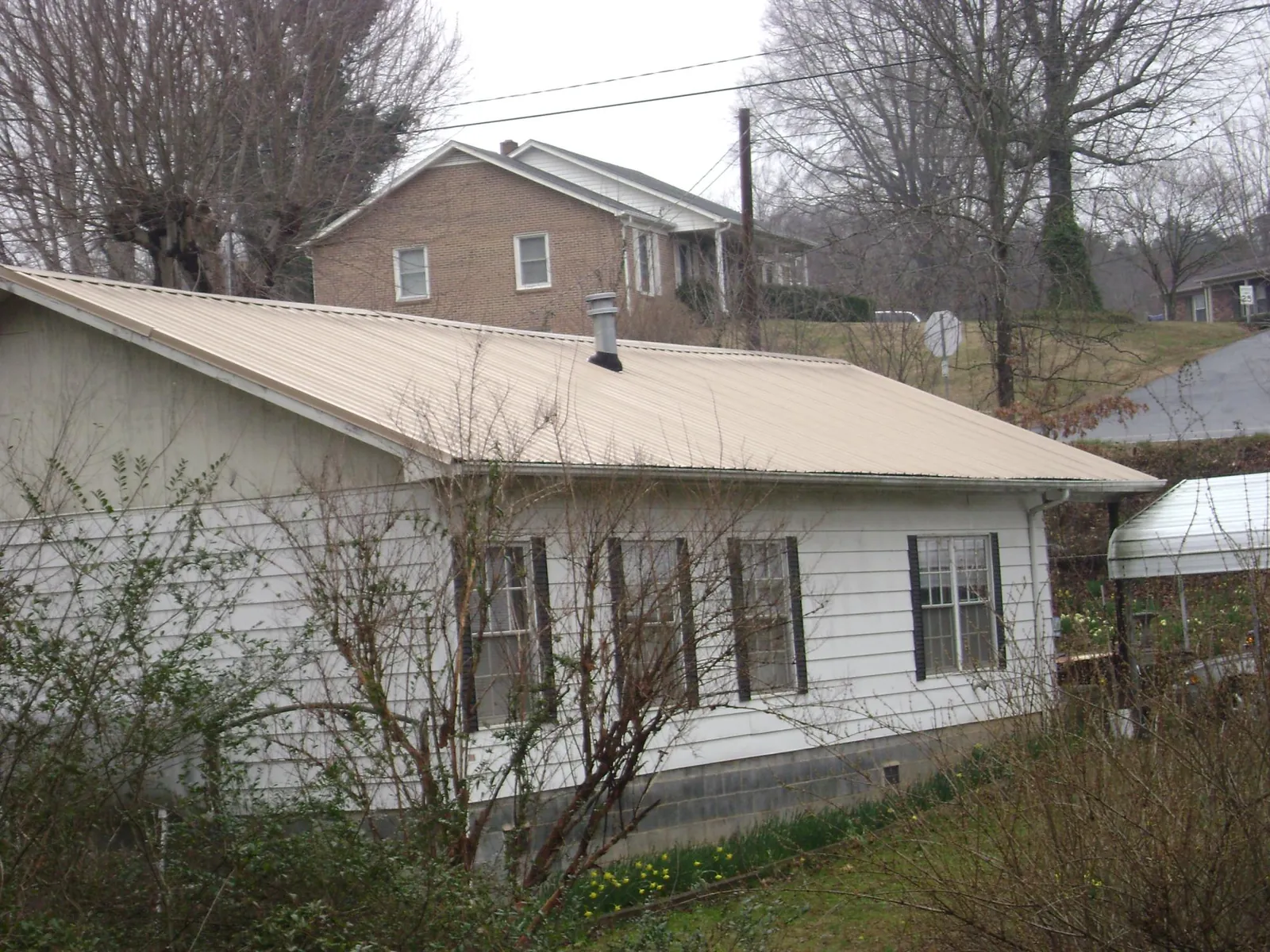 Tan metal roof on a white sided house set into a hillside — Commercial Roofing by Roofing Brothers in Asheboro