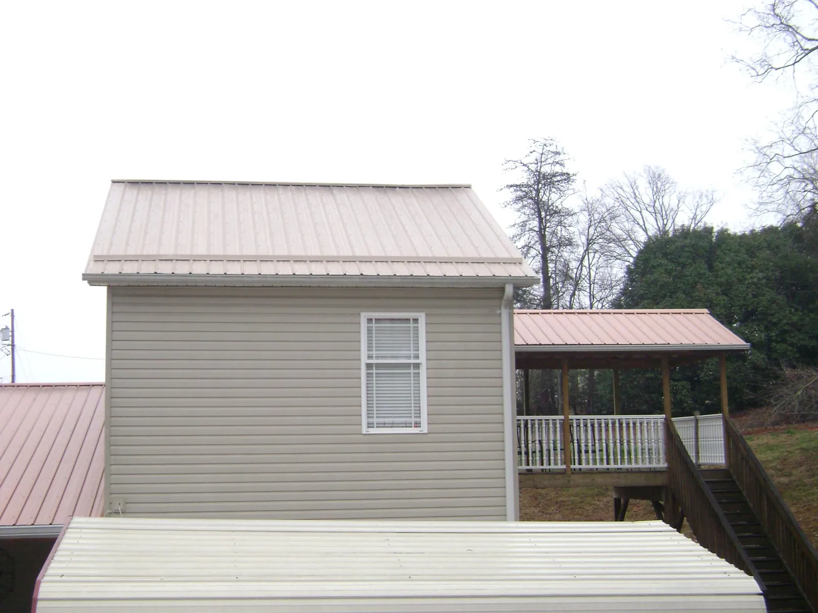 Tan metal roofs on a two story addition and attached porch, from a Roof Replacement job in Asheboro